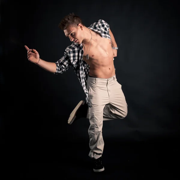 Studio portrait of dancing young man with plaid shirt against black background — Stock Photo, Image