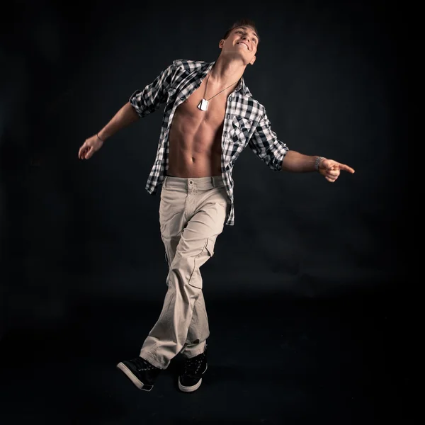 Studio portrait of dancing young man with plaid shirt against black background — Stock Photo, Image