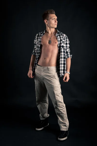 Studio portret van zelfverzekerde jonge man met plaid shirt tegen zwarte achtergrond — Stockfoto