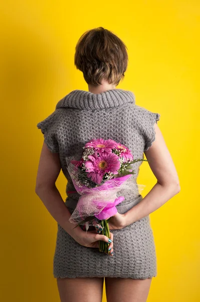 Back view Girl with gerbera flowers bouquet and wool dress against yellow background — Stock Photo, Image