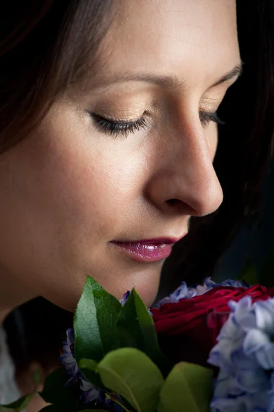 Portrait of beautiful woman smelling a flowers bouquet against black background — Stock Photo, Image