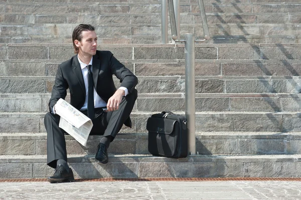 Young business man with newspaper sitting on the stairs — Stock Photo, Image