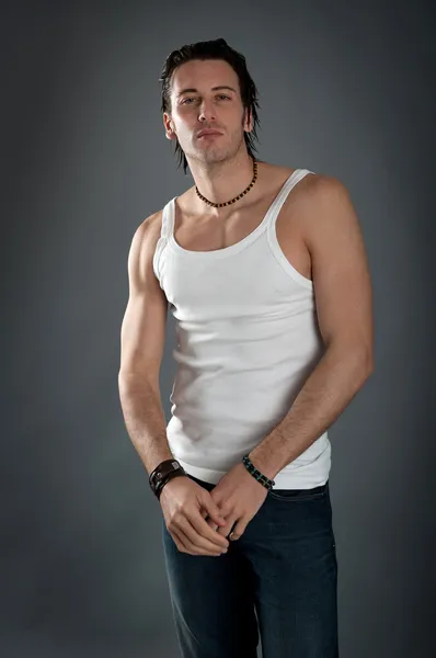 Athletic young man wearing jeans and white singlet against dark background — Stock Photo, Image