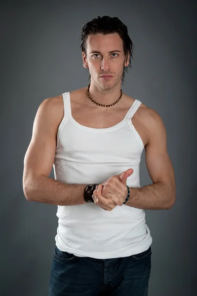 Athletic young man wearing jeans and white singlet against dark background — Stock Photo, Image