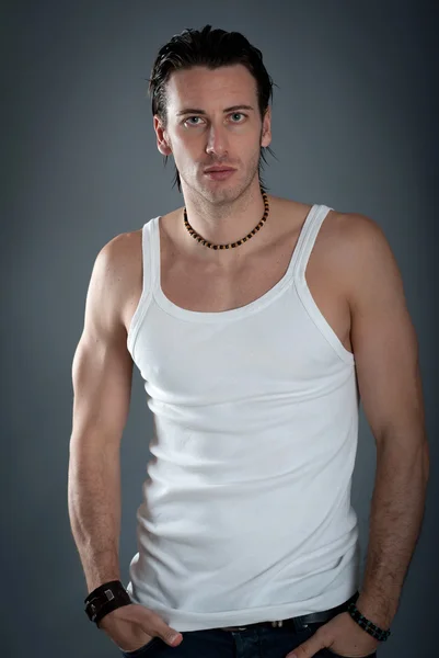 Athletic young man wearing jeans and white singlet against dark background — Stock Photo, Image