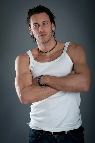 Athletic young man wearing jeans and white singlet against dark background — Stock Photo, Image