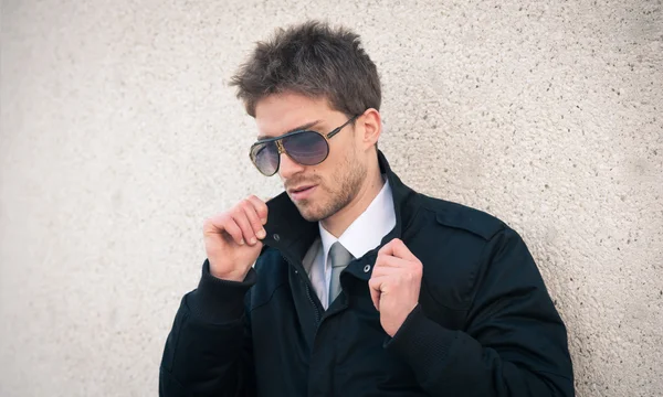Ung elegant man stående med solglasögon mot en vägg — Stockfoto