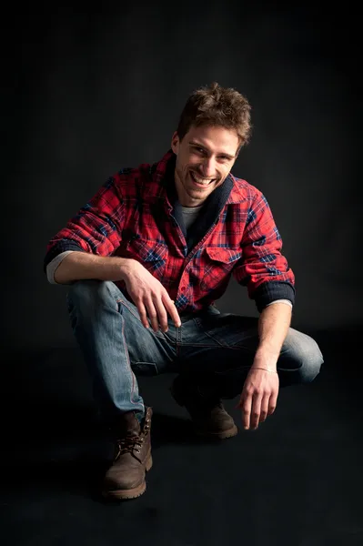 Portrait of young smiling man crouched against black background — Stock Photo, Image