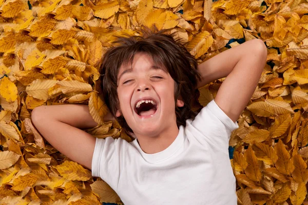 Enfant de 6 ans riant, allongé sur des feuilles d'automne — Photo