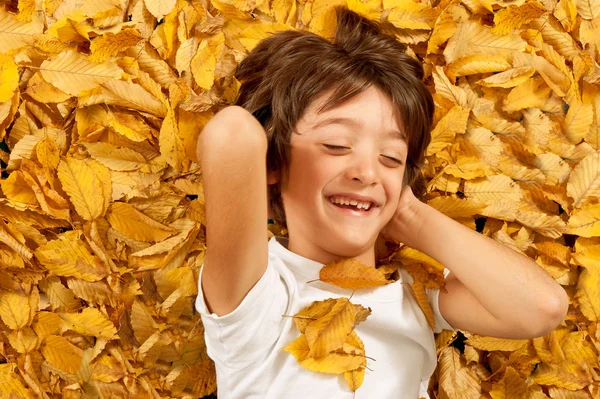 Enfant de 6 ans riant, allongé sur des feuilles d'automne — Photo