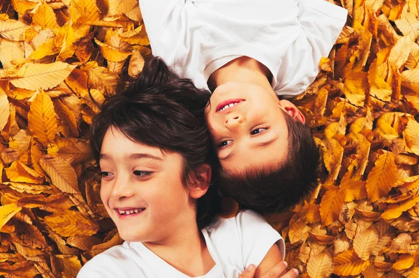 Two kids - 6 year old - laughing, lying on autumn leaves — Stock Photo, Image