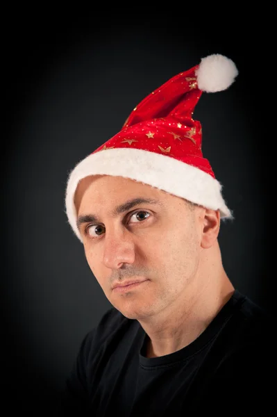 Homme à l'expression féroce et chapeau de Noël sur fond noir — Photo