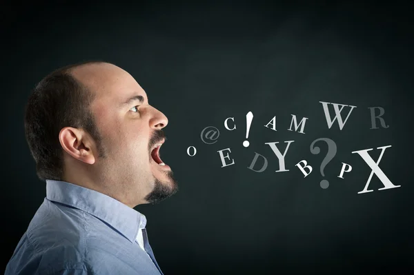 Homem irritado gritando contra fundo preto com letras vindas de sua boca — Fotografia de Stock