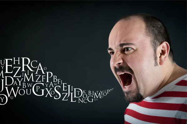 Angry man shouting against black background with letters coming — Stock Photo, Image