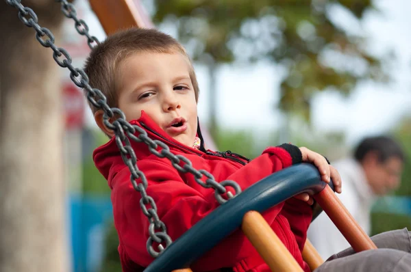 Niño de 3 años balanceándose en un día soleado con árboles en el fondo — Foto de Stock