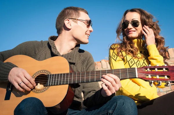 Romántico joven pareja retrato tocando la guitarra bajo el cielo azul —  Fotos de Stock