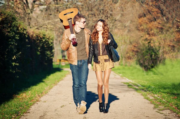 Young couple walking in a romantic mood with guitar outdoors in a park — Stock Photo, Image