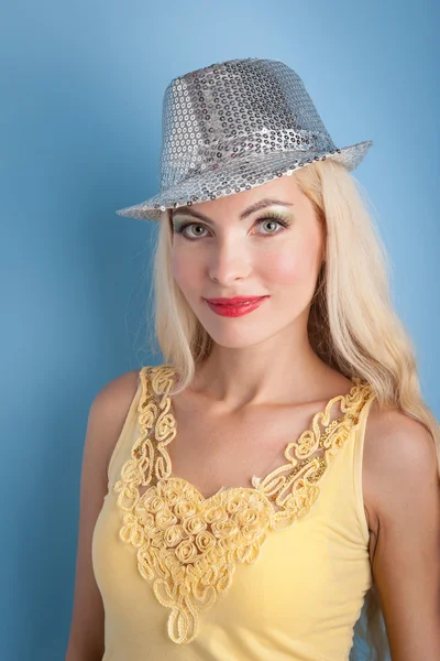 Blond meisje met glanzend zilver hoed tegen blauwe achtergrond — Stockfoto