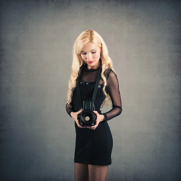 Beautiful blonde woman with medium format camera against dark background — Stock Photo, Image