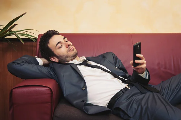 Retrato del joven hombre de negocios cansado escribiendo en el teléfono celular en el sofá —  Fotos de Stock