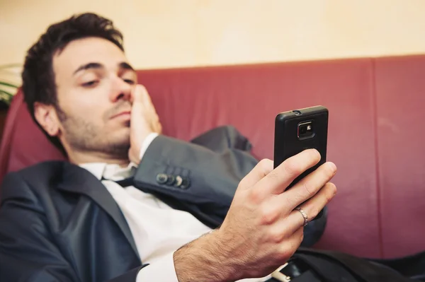 Портрет втомленого молодого бізнесмена, що друкує на мобільному телефоні на дивані — стокове фото