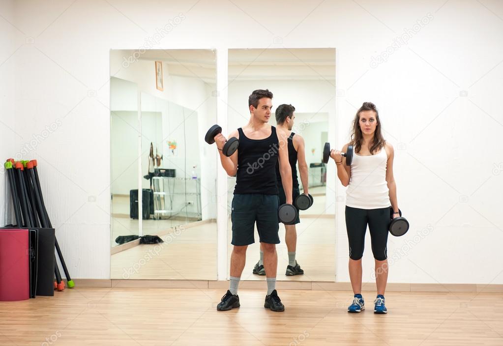 Young couple exercising with dumbbells at the gym