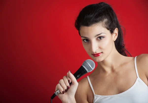 Schönes Mädchen singt mit Mikrofon vor rotem Hintergrund — Stockfoto