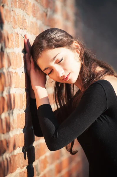 Jonge mooie ballerina buitenshuis poseren met gesloten ogen langs een bakstenen muur — Stockfoto