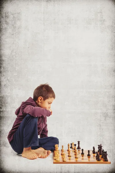 Kid (6 year old) playing chess, isolated on grunge background — Stock Photo, Image