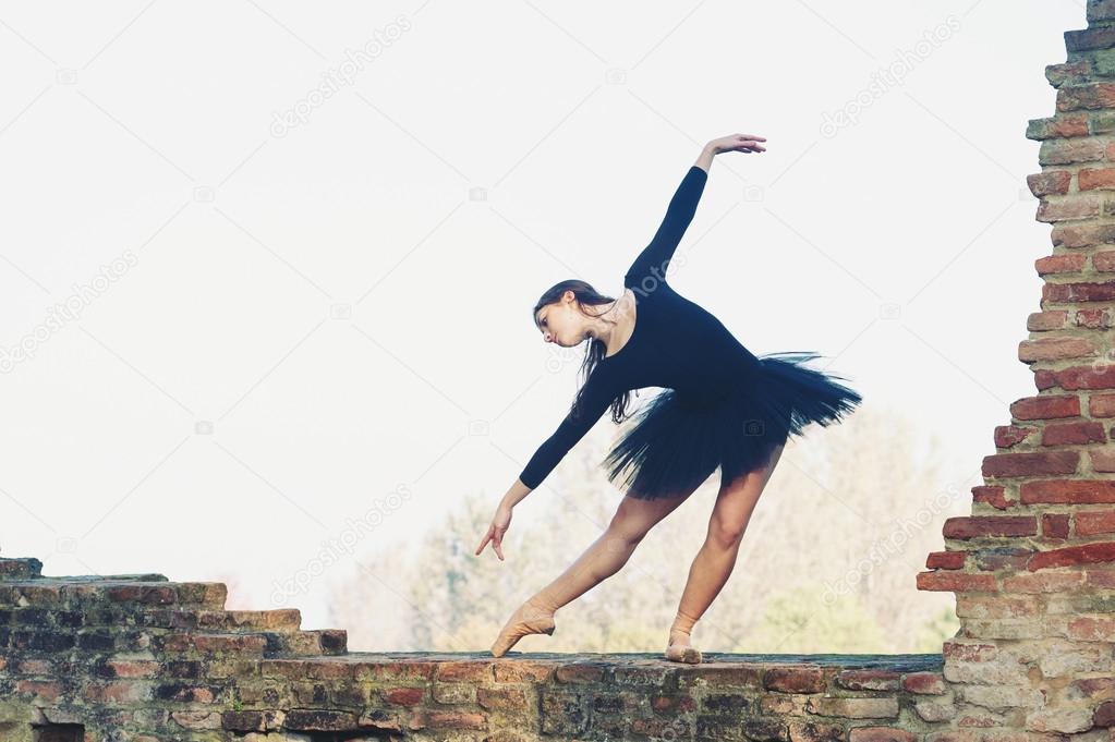 Young beautiful ballerina dancing outdoors on the brick wall