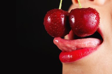 Detail of young woman mouth with cherries against black background clipart