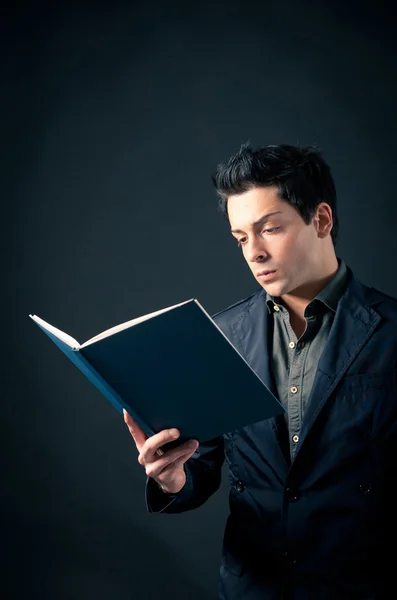 Junger Mann liest ein Buch vor dunklem Hintergrund — Stockfoto