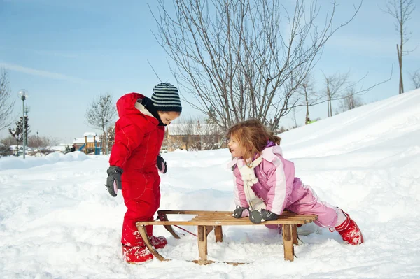 Två små barn - pojke och flicka - ha kul med släden i snön — Stockfoto