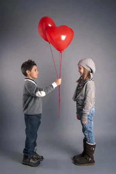 Kleines liebevolles Kinderpaar mit roten Herzballons auf grauem Hintergrund — Stockfoto