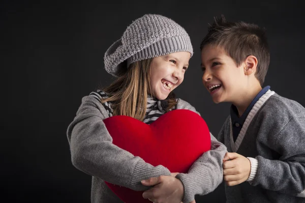 Couple of kids having fun with red heart over black background — Stock Photo, Image