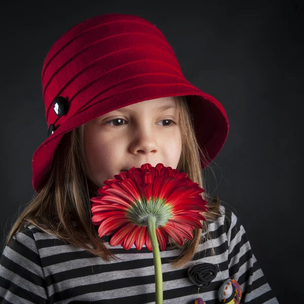 Little girl smells red daisy flower against black background — Stock Photo, Image