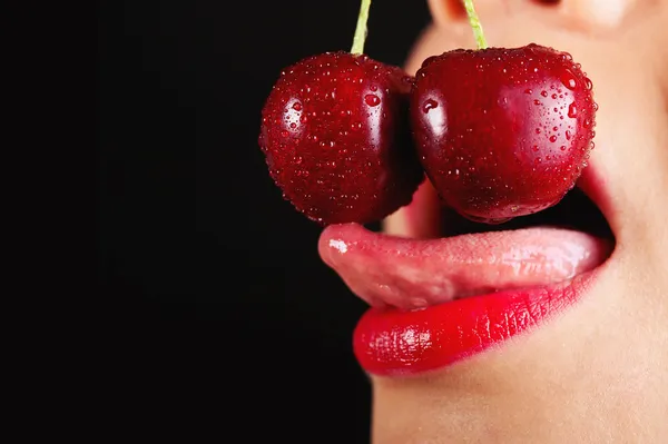 Detalle de boca de mujer joven con cerezas sobre fondo negro — Foto de Stock