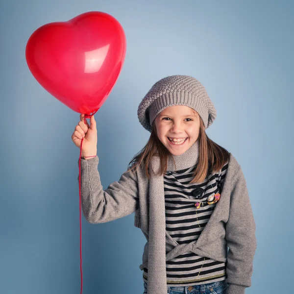 Menina sorridente nova com balão de coração vermelho no fundo azul . — Fotografia de Stock