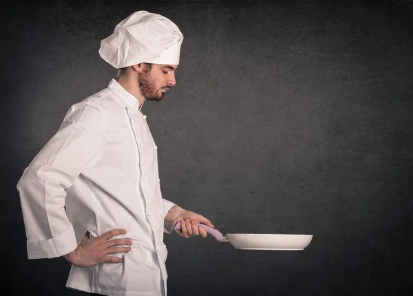 Portrait of a young cook man with pan wearing uniform over grunge background — Stock Photo, Image