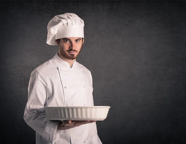 Joven cocinero con uniforme llevando estaño para hornear sobre grunge espalda — Foto de Stock