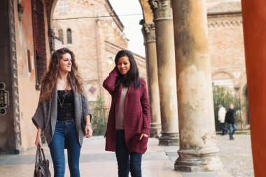 Two girls walking outdoors in Saint Stephen square, Bologna, Italy. clipart