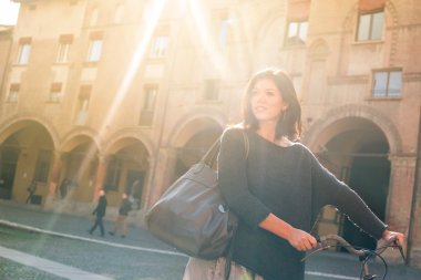 Woman walking with bicycle in Saint Stephen square, Bologna, Italy. Back light.
