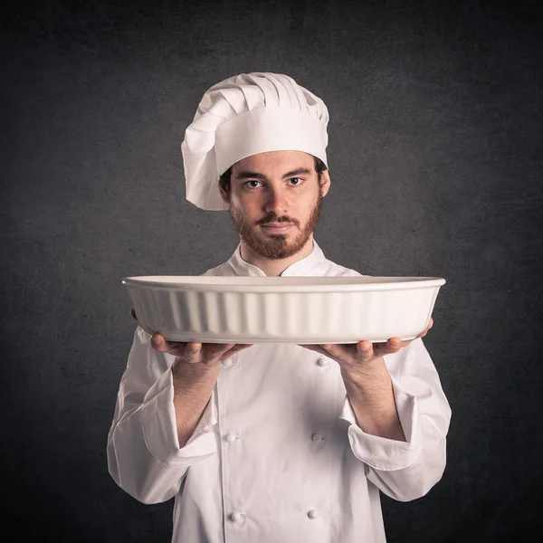 Young cook man with uniform showing baking tin over grunge background. — Stock Photo, Image