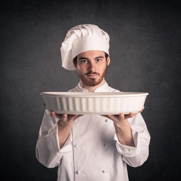 Joven cocinero con uniforme mostrando hojalata sobre fondo grunge . — Foto de Stock