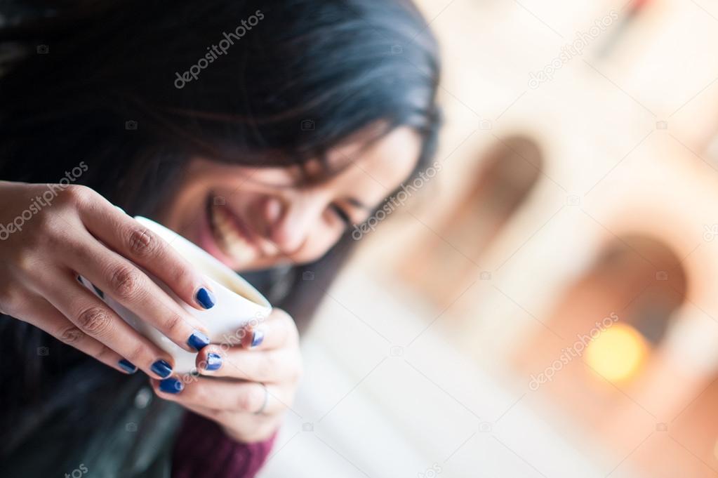 Laughing woman drinking coffee in a cafe outdoors. Focus on hands. Shallow depth of field.