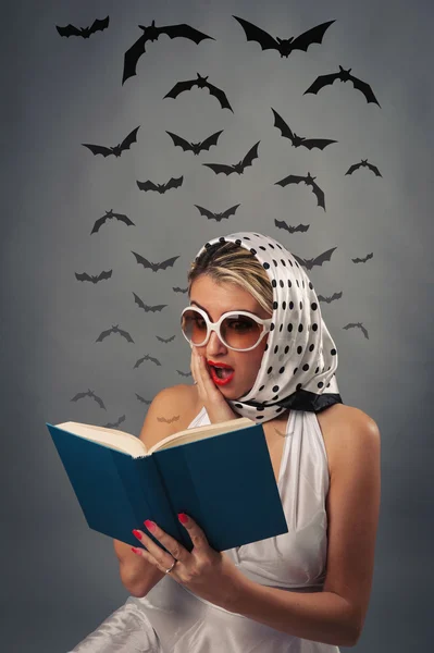 Rädd retro kvinna läser bok med fladdermöss silhuetter mot mörk bakgrund. — Stockfoto