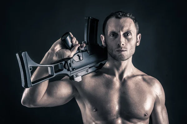 Confident young man shirtless portrait with machine gun against black background. — Stock Photo, Image