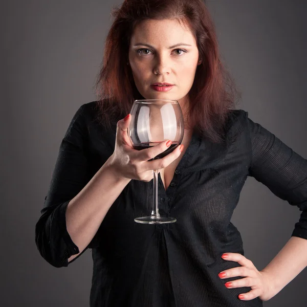 Mulher com copo de vinho tinto na mão sobre fundo cinza . — Fotografia de Stock