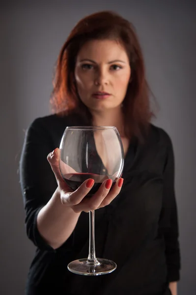 Frau mit einem Glas Rotwein in der Hand auf grauem Hintergrund. geringe Schärfentiefe. — Stockfoto