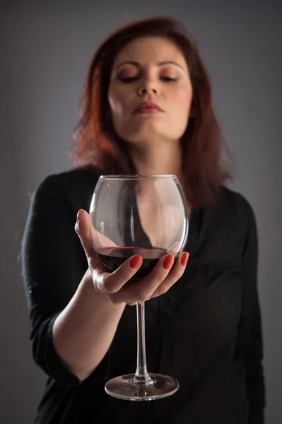 Frau mit einem Glas Rotwein in der Hand auf grauem Hintergrund. geringe Schärfentiefe. — Stockfoto